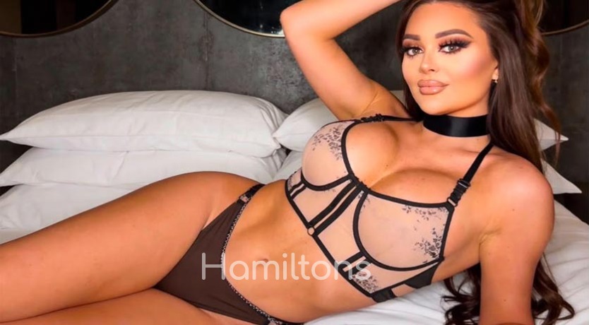 Beth lying on a bed in sheer lingerie and a choker